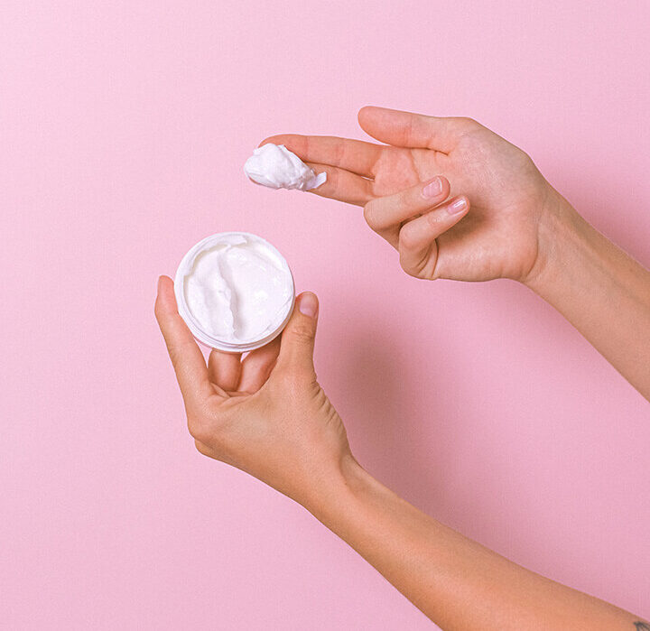Hands with a small pot of moisturizing cream