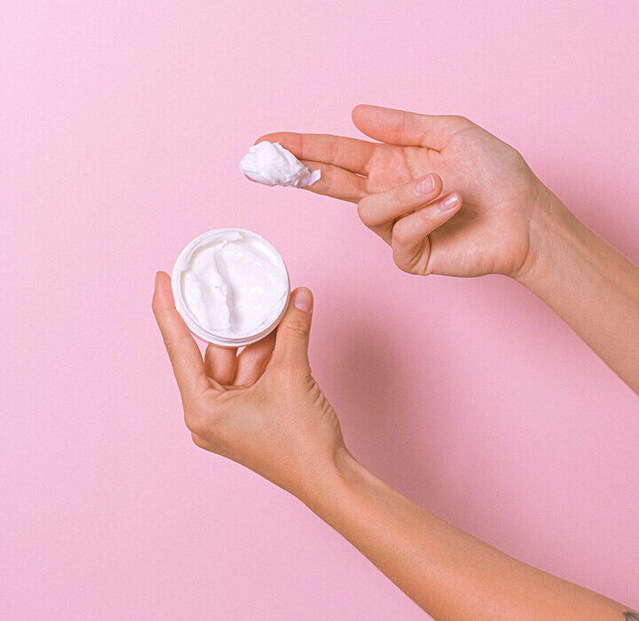 Hands with a small pot of moisturizing cream